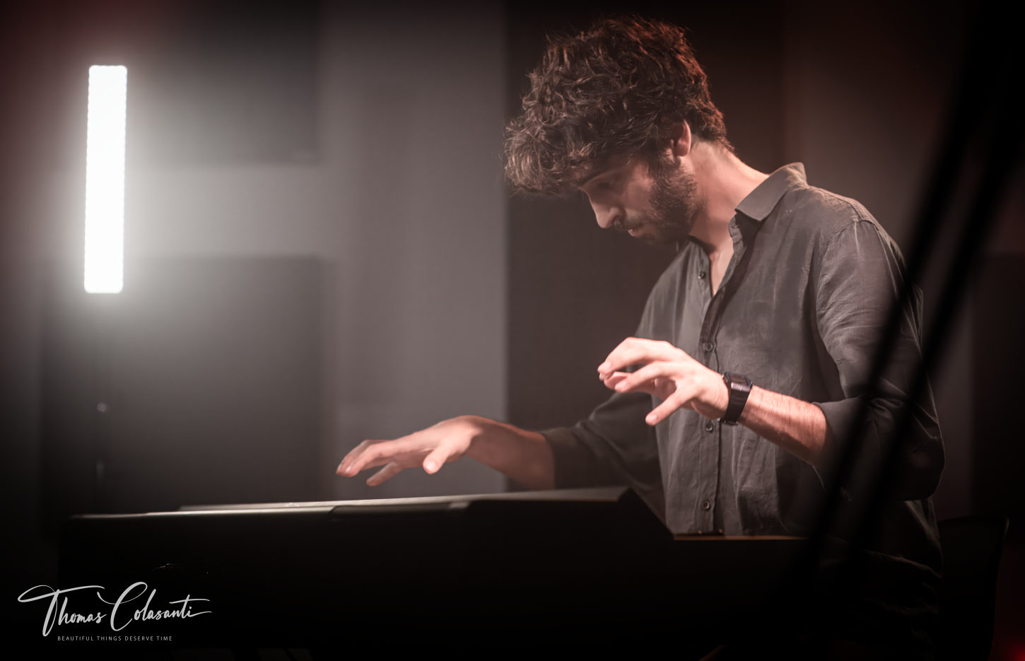 Pianista di profilo davanti ai tasti, mani sospese in controluce durante una sessione in studio.