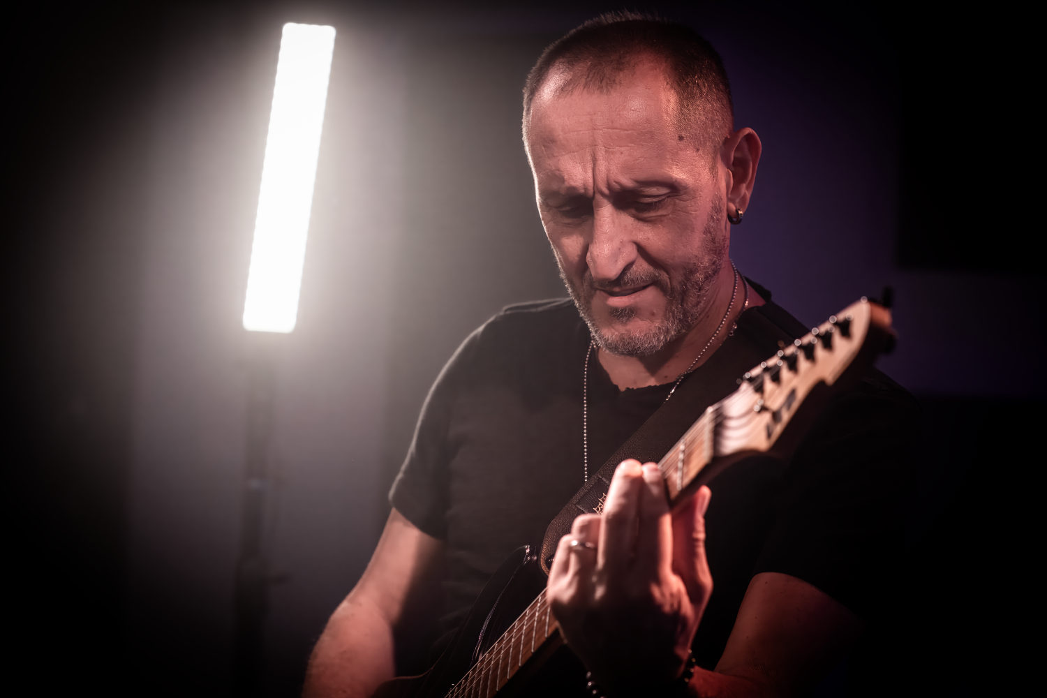 Chitarrista durante una sessione fotografica in studio, mani sul manico della chitarra elettrica, inquadratura ravvicinata.