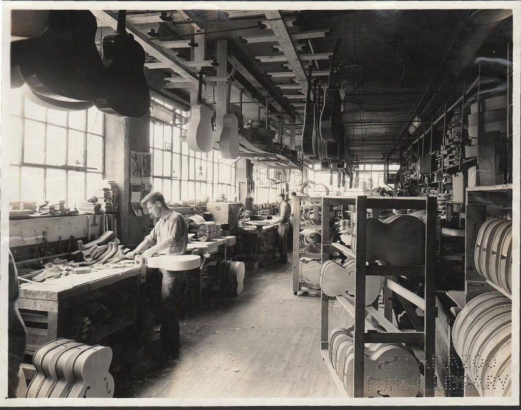 Sala di assemblaggio generale della Gibson di Kalamazoo nel 1936, uomini al lavoro sui banchi fra corpi di chitarra su carrelli