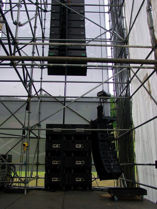 Sistema PA di metà anni Duemila con line array sospeso, subwoofer e ground stack disposti a terra sul lato del palco