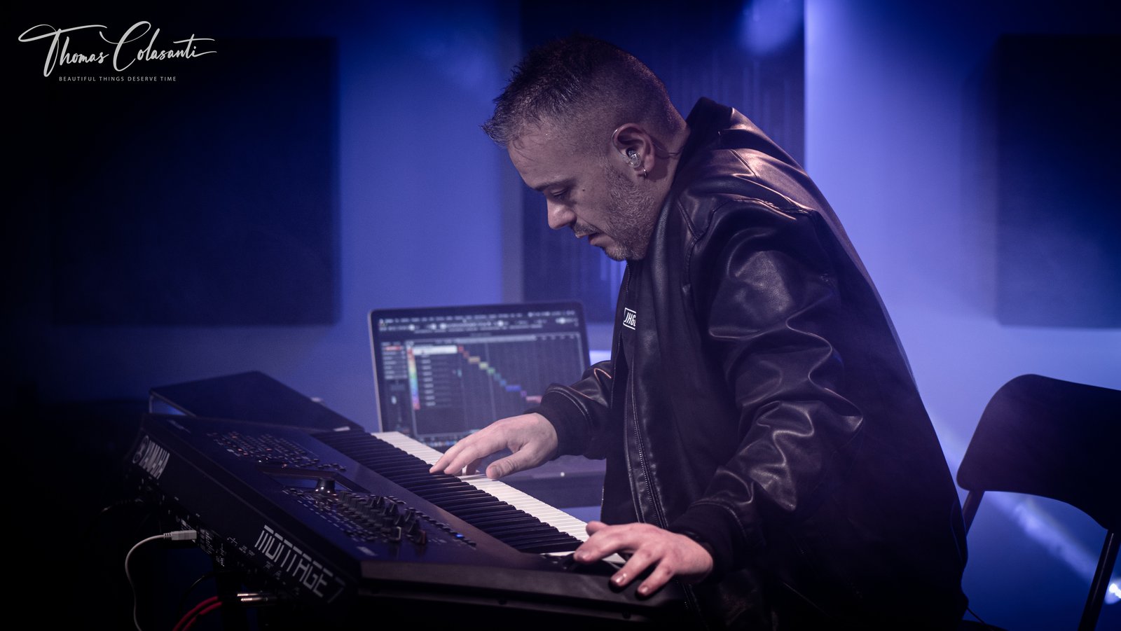 Manuele Montesanti di profilo suona una Yamaha Montage 7 con lo sguardo rivolto ai tasti, un laptop con la sessione aperta alle spalle e luci di scena blu