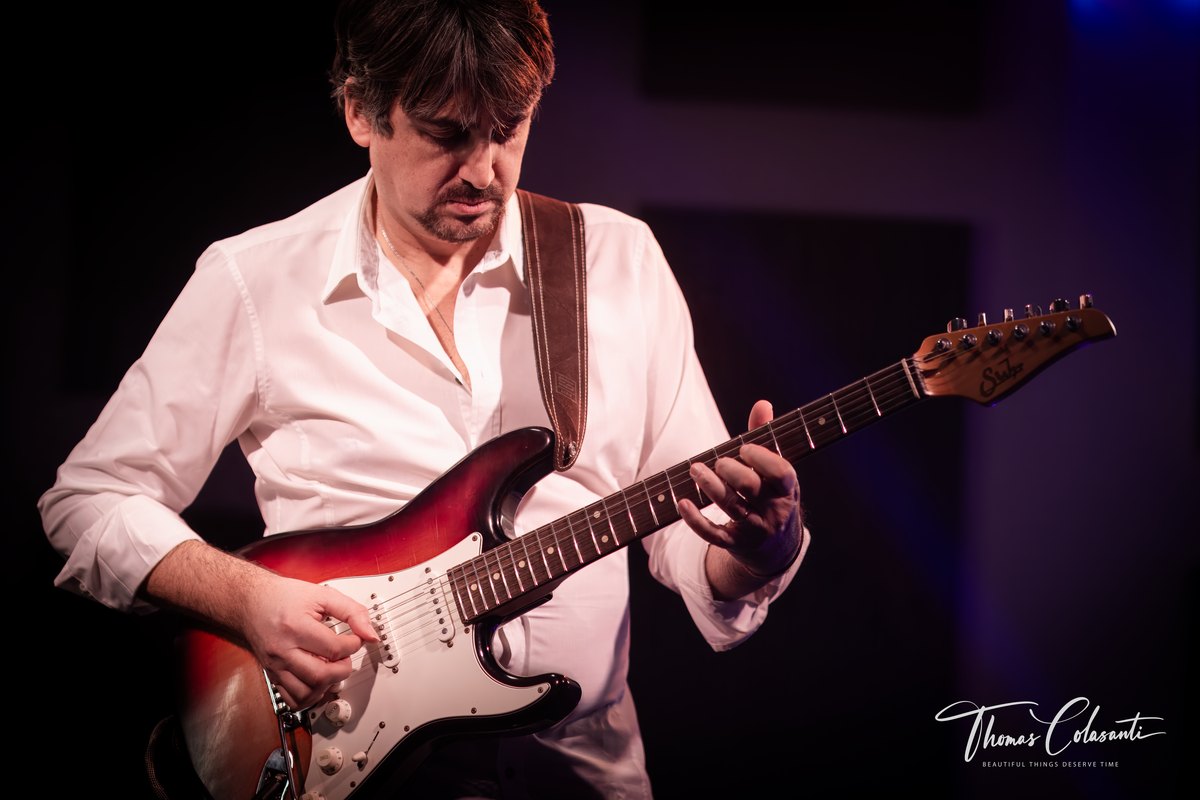primo piano di chitarra elettrica dal corpo sunburst con paletta chiara, mano sul manico e sguardo rivolto verso il basso