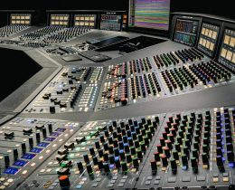 Console analogica SSL Odyssey da 48 canali vista di tre quarti, con le strisce di canale e la sezione centrale illuminate