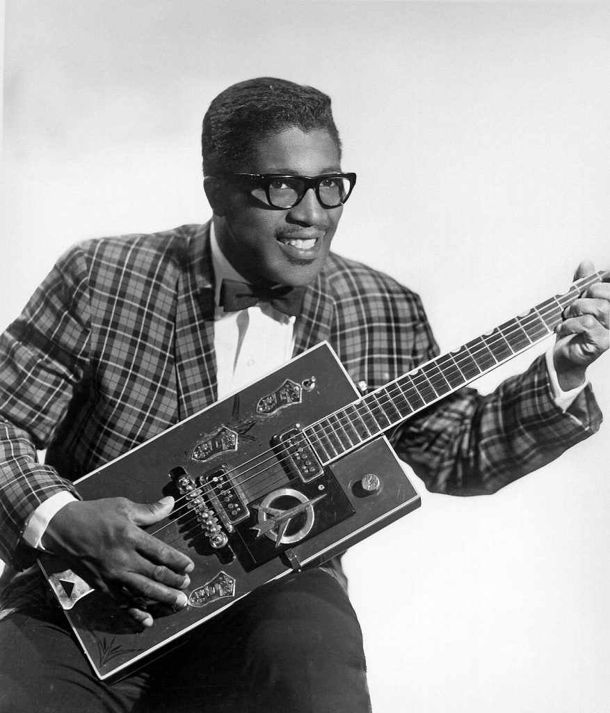 Bo Diddley seduto con la sua chitarra elettrica dal corpo rettangolare in una foto promozionale del 1957