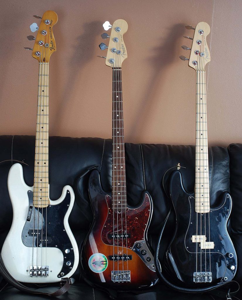 Tre bassi Fender appoggiati a un divano scuro, due Precision Bass ai lati e un Jazz Bass sunburst con battipenna tartarugato al centro