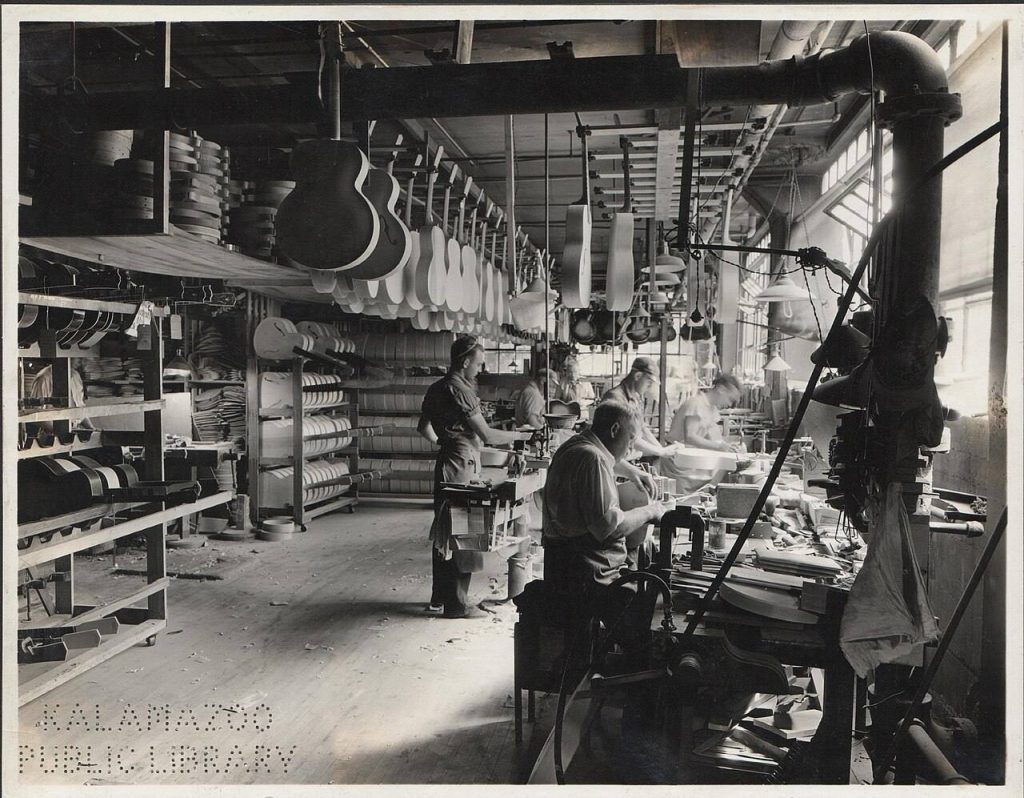 Operai al banco nel reparto chitarre dello stabilimento Gibson di Kalamazoo nel 1936, con casse e fasce appese al soffitto