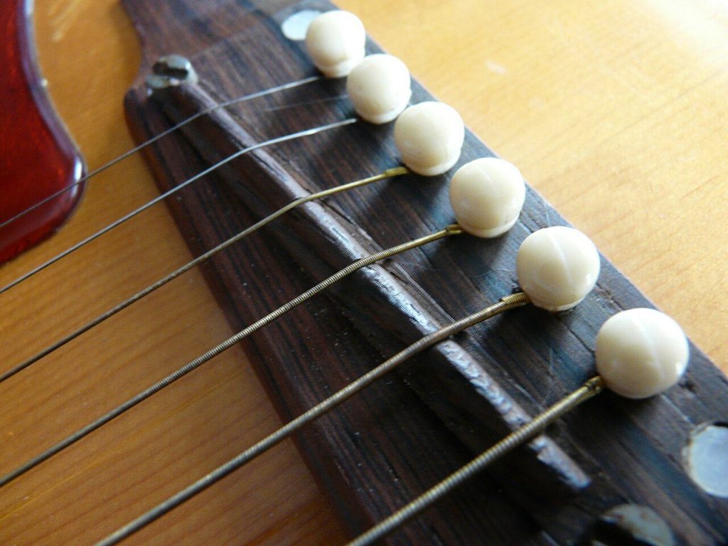 Dettaglio ravvicinato del ponte in legno di una Gibson J-50, con i pin delle corde in vista e le corde tese sopra la selletta